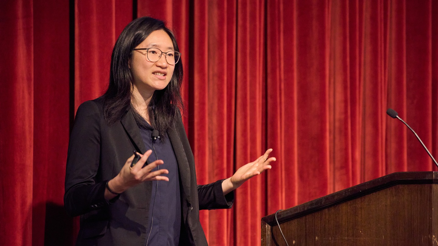 Angela Shou presents in front of the curtain.