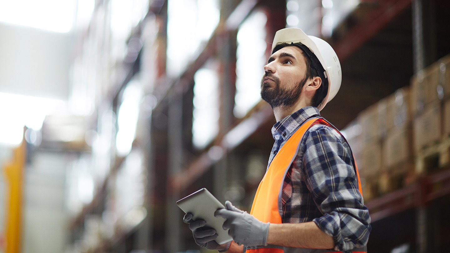 Male-presenting worker in a warehouse holding an iPad.