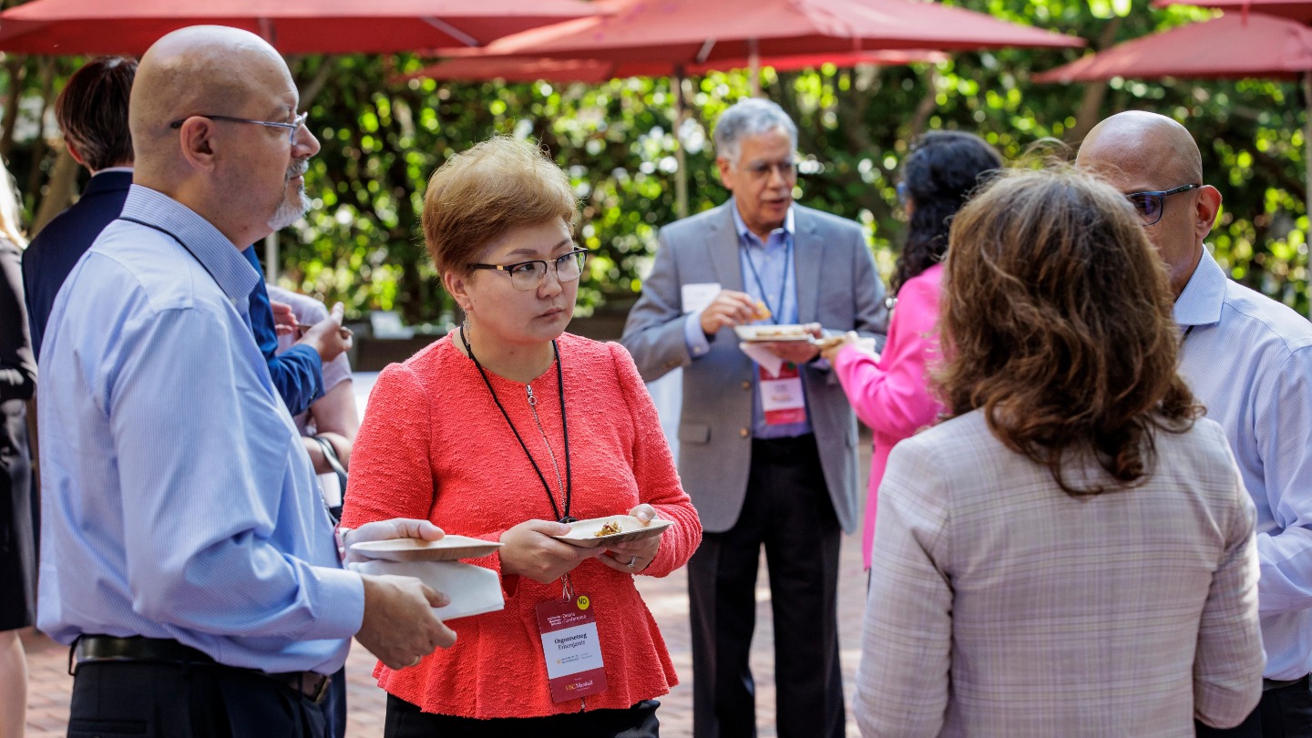 A group of deans discuss something on the Annenberg patio while holding small plates.
