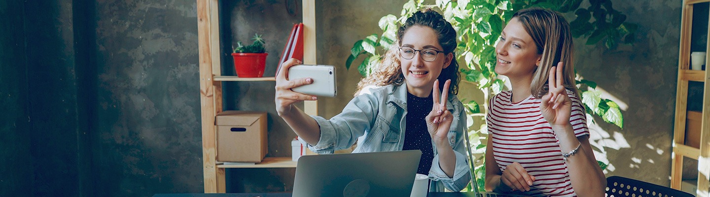 Two female-presenting students taking a selfie and showing the &quot;Fight On!&quot; handsign.
