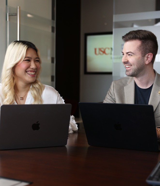 Two smiling graduate students in front of laptops