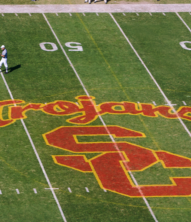 A photo of the USC logo on the football field with the word &quot;Trojans&quot; above it.