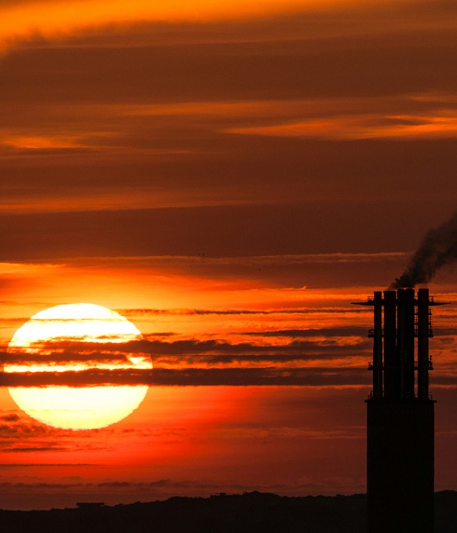 Large sun on a long zoom at sunset with a silhouette of a refinery.