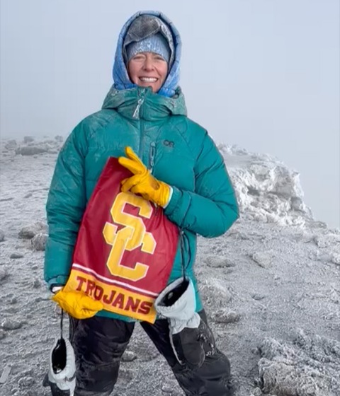 Color photograph of woman holding a USC flag at the top of Mount Kilimanjaro.