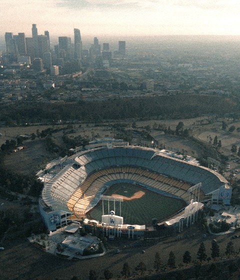 Color aerial photograph of Dodger Stadium with downtown Los Angeles in the background.