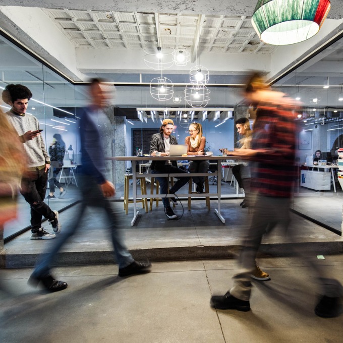 A man and a woman sit and talk at a table while people walk by them.