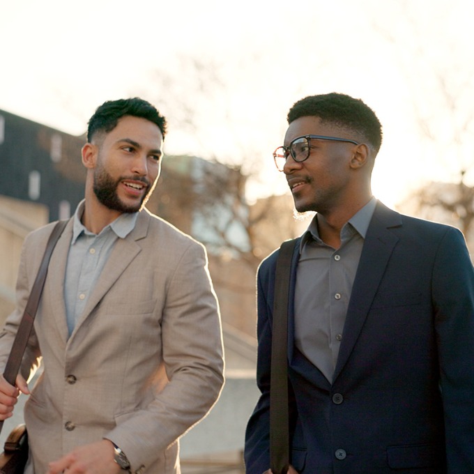 Two people in business casual attire walking outdoors near sunset.
