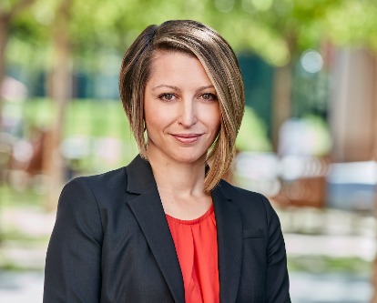 White woman wearing blue jacket over orange blouse, standing outdoors