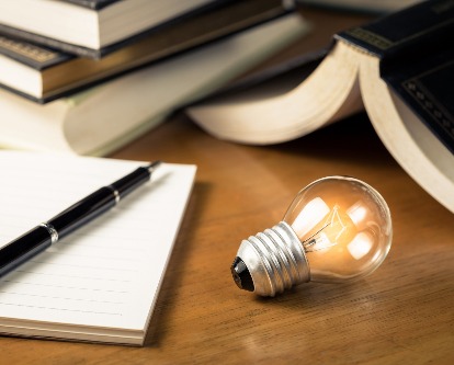 Desk table with pen and journal and a lit light bulb, signifying new ideas