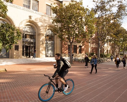 Bicyclist and pedestrians stroll on campus past the Leventhal School building