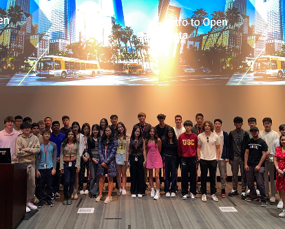 A group of high school students stand in front of a large screen as part of their data analytics program.
