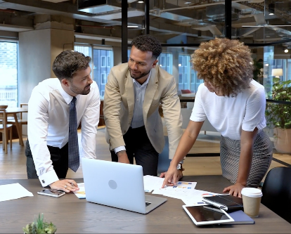 Three co-workers work on a project while pointing at papers on a desk.