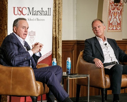 Color photograph of two men in conversation wtih USC Marshall banner