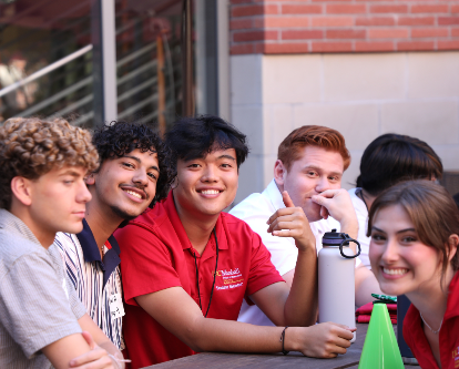 Students smiling at a table outside.