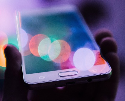 Color photograph, slightly out of focus, of a hand holding an iPhone.