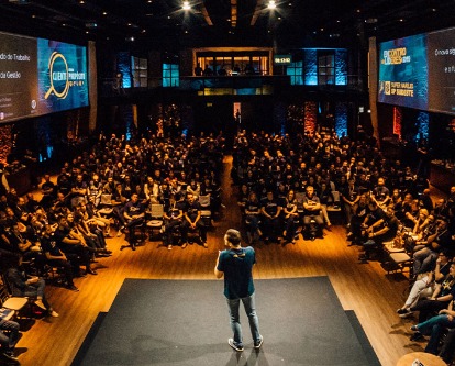 Color photo showing a speaker in front of a large audience.
