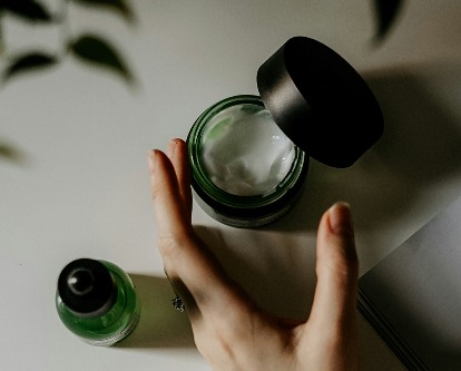A hand reaching for a jar of cosmetic lotion.