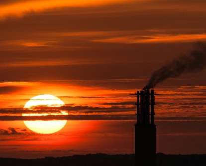 Large sun on a long zoom at sunset with a silhouette of a refinery.