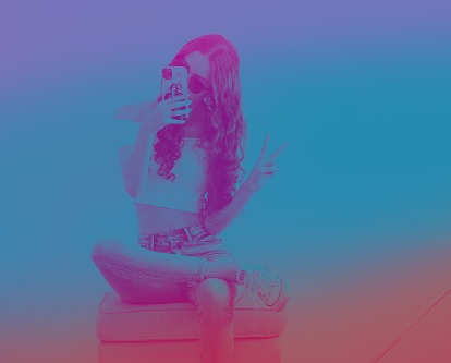 Female-presenting social influencer on a phone flashing the &quot;peace&quot; sign.