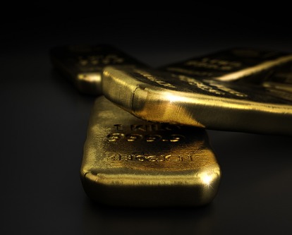 Color photograph of three gold bars laying on a dark, black set.