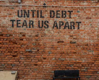 Brick wall with "Until Debt Tear Us Apart" stenciled in black.