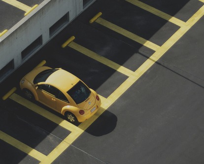 A yellow VW bug parked in an empty black lot with yellow striping.