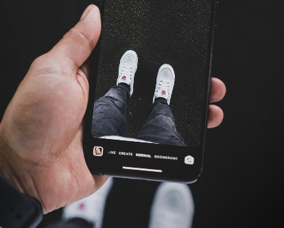 POV of a hand holding a phone and taking photo of their shoes.