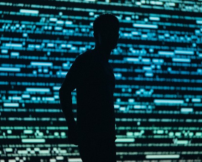 Color photograph of a person silhouetted against a blue and green digital backdrop.