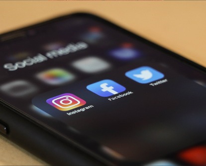 Color photograph of a smartphone displaying icons for Instagram, Facebook, and Twitter.