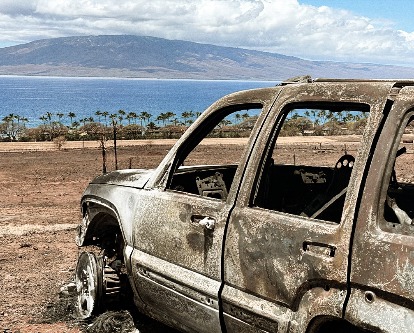 Color photograph of a car burnt down to the frame following the Maui fires of 2023.