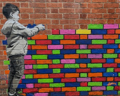 Banksy-esque mural on a brick wall depicting a young boy stacking colored bricks.