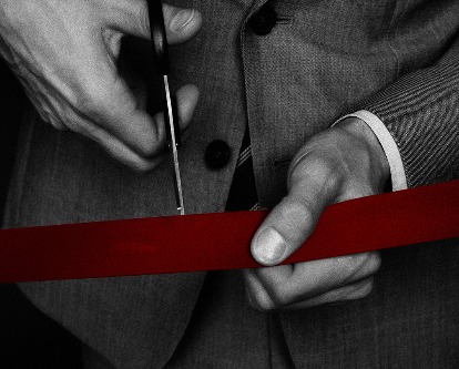 Hands taking scissors to red tape.