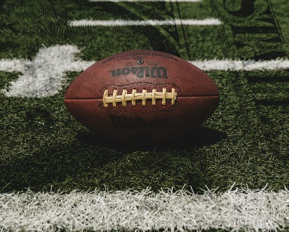 Football sitting on a field with dollar bill superimposed.