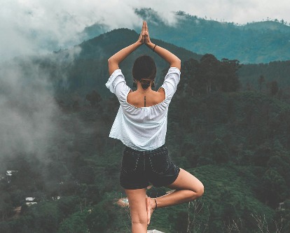Woman performing tree pose in a mountain setting.