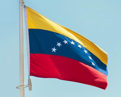 Color photograph of the Venezuelan flag set against a blue sky.