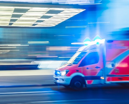 Color photograph of an ambulance driving with flashing lights.