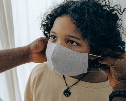 Color photograph of an adult putting a face mask on a child.