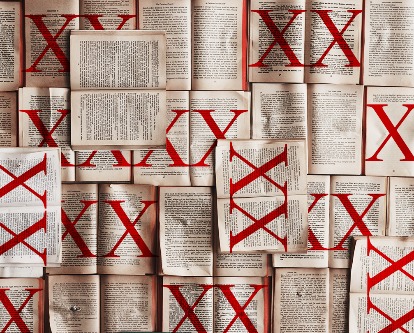 Color image looking down at dozens of books open - many of which have red crosses over them to imply they've been banned.