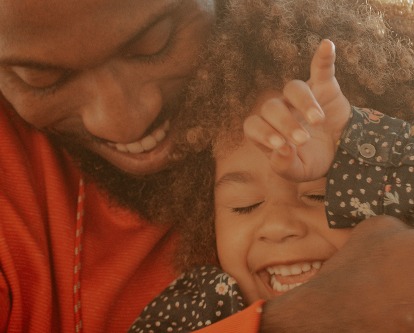 Color photograph of a father and young child cuddling and smiling.
