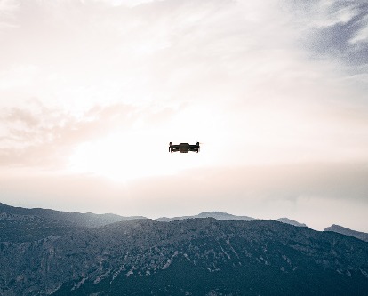 Color photograph of a drone flying over a mountain range on a partially cloudy day.