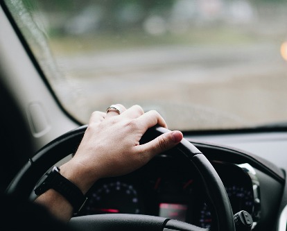 A hand on the steering wheel of a car.