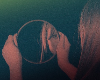 A woman holding and looking into a round mirror.