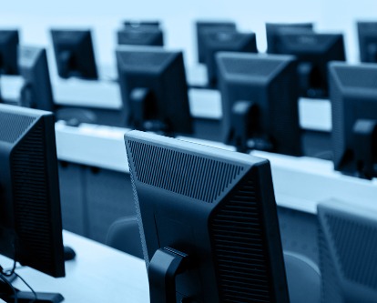 Color photograph of multiple rows of computer monitors in an office.