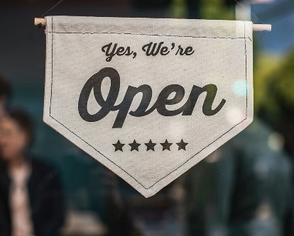 A sign reading &quot;Yes, We're Open&quot; in the window of a small business.