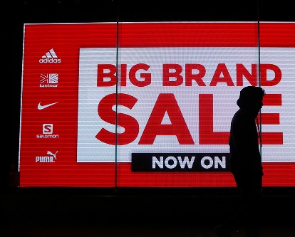 Walker silhouetted against a red sign reading &quot;Big Brand Sale&quot;.