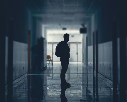 Silhouette of a student standing in an empty school hallway.