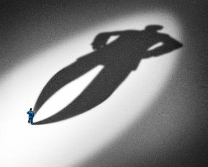 A male-presenting executive stands looking at his oversized cast shadow.