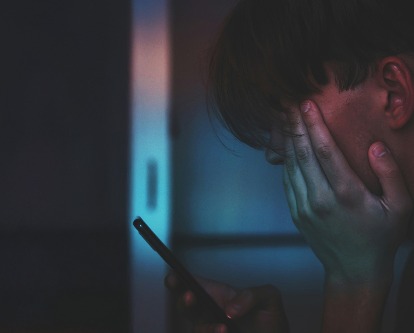 A male-presenting teen scrolling on a smart phone.