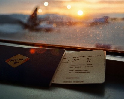 An airplane boarding pass and passport in the window of a terminal looking out towards the sun setting on the tarmac.