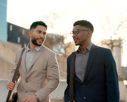 Two people in business casual attire walking outdoors near sunset.